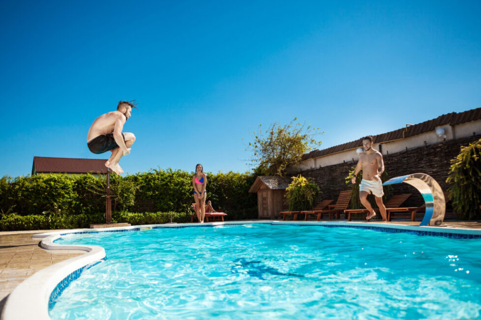 Young cheerful friends smiling, relaxing, jumping in swimming pool.